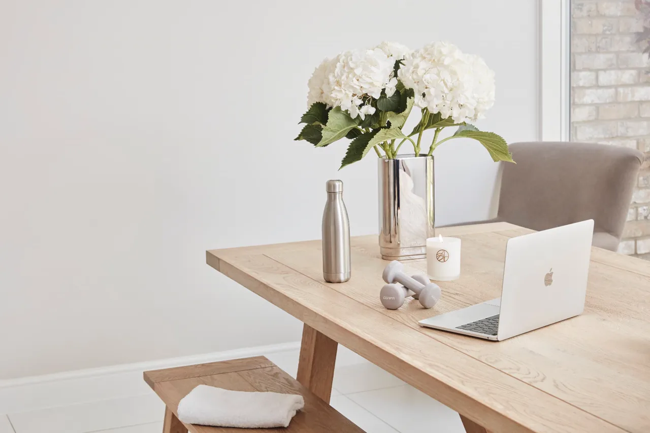 A calm home wellness space with a laptop, hand weights and water bottle